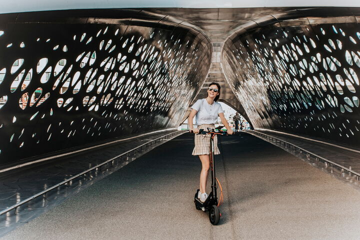 Dame op een e-step met de Parkbrug als decor. 