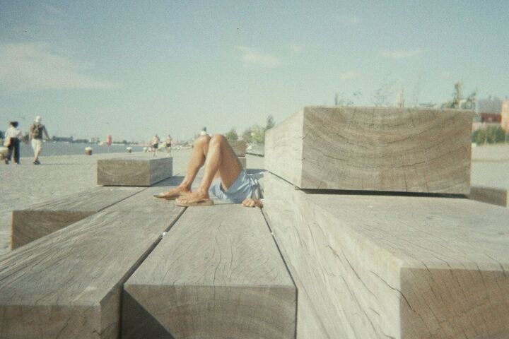 Houten zitbanken aan de Scheldekaaien op een zonnige promenade met voorbijgangers op de achtergrond.